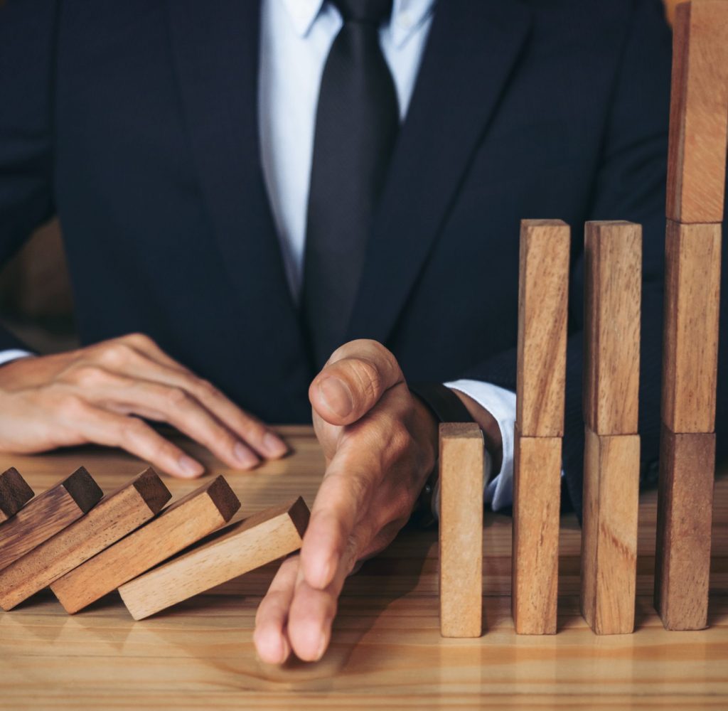 Close up of businessman hand Stopping Falling wooden Dominoes effect from continuous toppled or risk, strategy and successful intervention concept for business.